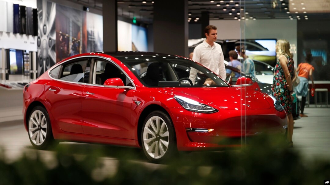 FILE- In this July 6, 2018, file photo, a prospective customer confer with sales associate as a Model 3 sits on display in a Tesla showroom in the Cherry Creek Mall in Denver. 