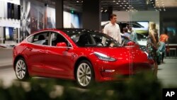 FILE- In this July 6, 2018, file photo, a prospective customer confer with sales associate as a Model 3 sits on display in a Tesla showroom in the Cherry Creek Mall in Denver. 