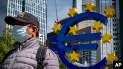 FILE - A man walks by an artistic representation of Europe's euro currency sign, in front of the old the European Central Bank in Frankfurt, Germany, May 5, 2020.
