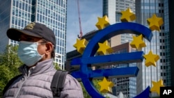 FILE - A man walks by an artistic representation of Europe's euro currency sign, in front of the old the European Central Bank in Frankfurt, Germany, May 5, 2020.