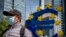 FILE - A man walks by an artistic representation of Europe's euro currency sign, in front of the old the European Central Bank in Frankfurt, Germany, May 5, 2020.