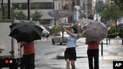 Passers-by try to manage their umbrellas in rain and strong wind generated by tropical storm Muifa in downtown Seoul, South Korea, Aug. 8, 2011.