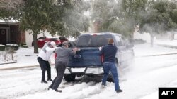 Residentes ayudan al conductor de una camioneta a salir del hielo en la carretera en Round Rock, Texas, el 17 de febrero de 2021, después de una tormenta invernal. 