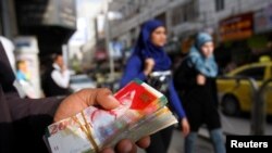 FILE - Palestinian women walk past a money changer in the West Bank city of Ramallah, Feb. 16, 2010.