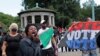 Holding a sign that reads, "The American system is rigged," a woman amplifies her voice as she implores protesters to rise to the occasion and become activists during a Caribbean-led Black Lives Matter rally at Brooklyn's Grand Army Plaza.