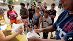 Los inmigrantes que buscan asilo en Estados Unidos reciben desayuno de un grupo de voluntarios en el puente internacional, en Matamoros, México.