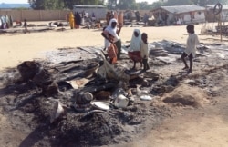 FILE - People stand amid the damage at a camp for displaced people after an attack by suspected members of the Islamist Boko Haram insurgency in Dalori, Nigeria, Nov. 1, 2018.