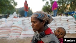 A woman carries an infant as she queues in line for food, at the Tsehaye primary school, which was turned into a temporary shelter for people displaced by conflict, in the town of Shire, Tigray region, Ethiopia, March 15, 2021.