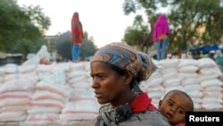 FILE - A woman carries an infant as she queues in line for food, at the Tsehaye primary school, which was turned into a temporary shelter for people displaced by conflict, in the town of Shire, Tigray region, Ethiopia, March 15, 2021.