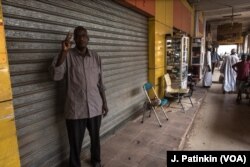 Siddig Ibrahim holds a V for Victory sign, a symbol of Sudan's revolution, outside his shuttered shop during the strike while one shop next door remains open, in Khartoum, Sudan, May 28, 2019.