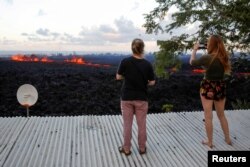 Jolon Clinton, 15, (L), and her sister, Halcy, 17, take photos of a fissure near their home on the outskirts of Pahoa during ongoing eruptions of the Kilauea Volcano in Hawaii, May 14, 2018.