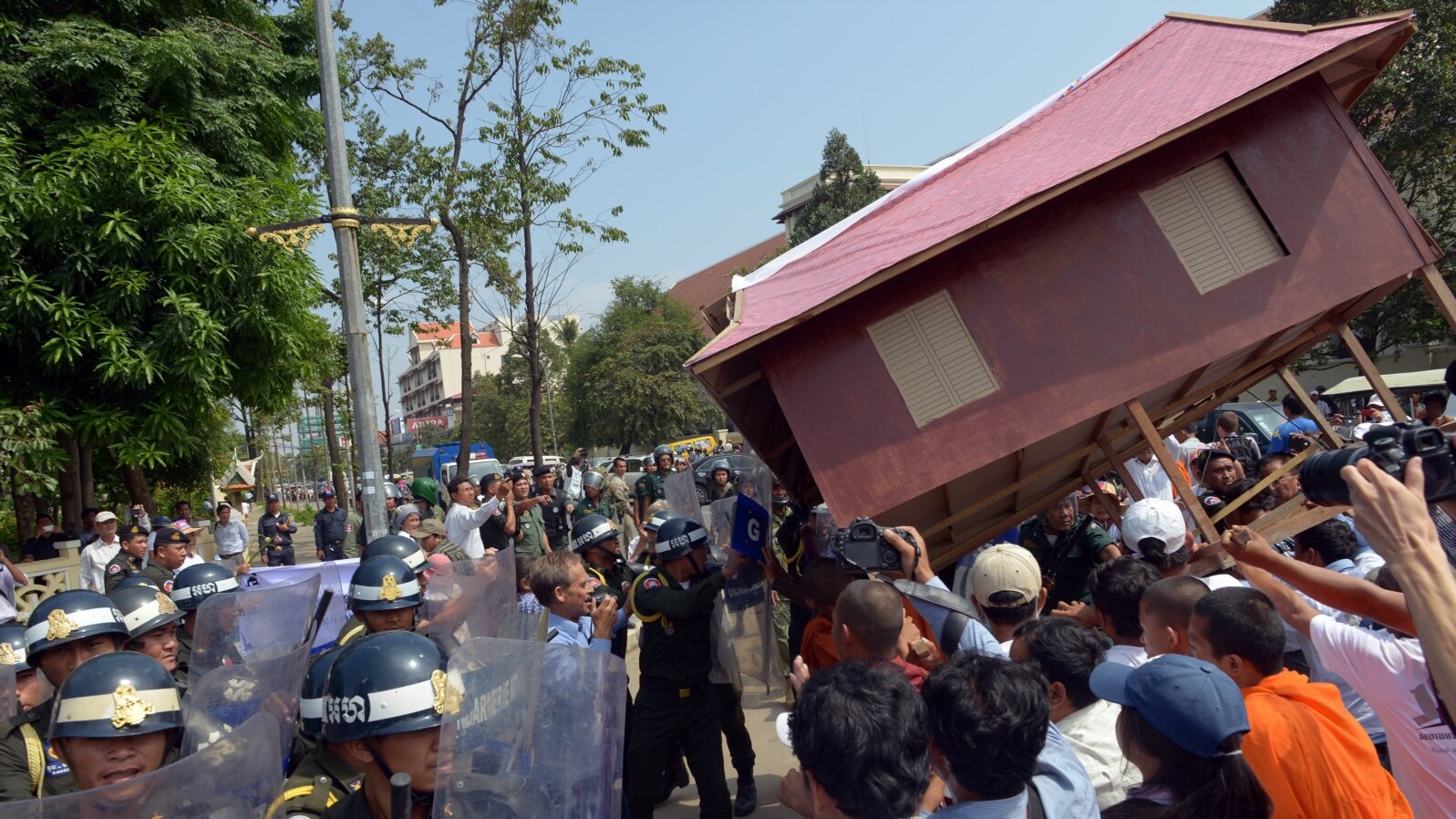 People carry a giant model of a house toward police as they protest government-sanctioned evictions, World Habitat Day, Phnom Penh, Oct. 10, 2013.