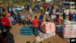 FILE - People affected by the coronavirus economic downturn receive food donations at the Iterileng informal settlement near Laudium, southwest of Pretoria, South Africa, May 20, 2020.