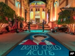 Penari Aztec berdiri di dekat tapete (karpet serbuk gergaji tradisional) bergambar Beato Carlo Acutis, pada perayaan Dia de Los Muertos di East Los Angeles, Minggu, 1 November 2020. (Damian Dovarganes/AP)