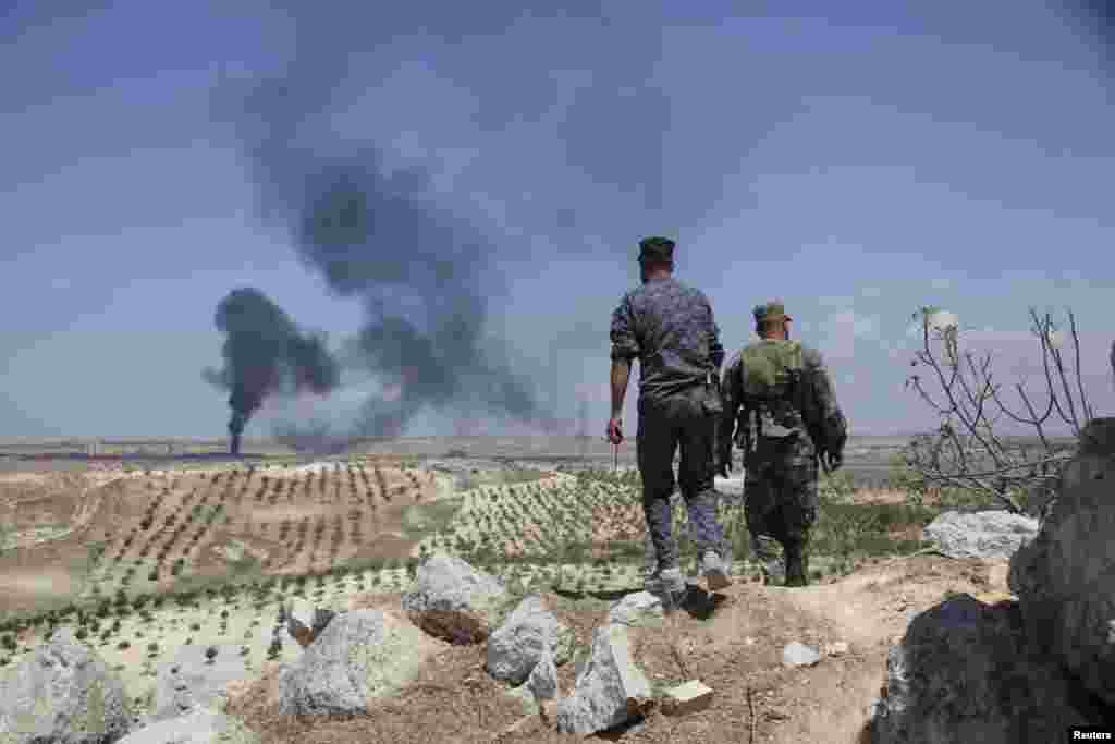 Syrian army soldiers loyal to President Bashar al-Assad walk on Hilan Hill. Syrian army reports claim that the smoke rising from a nearby village was a result of shelling by Syrian warplanes, near Aleppo, May 21, 2014.
