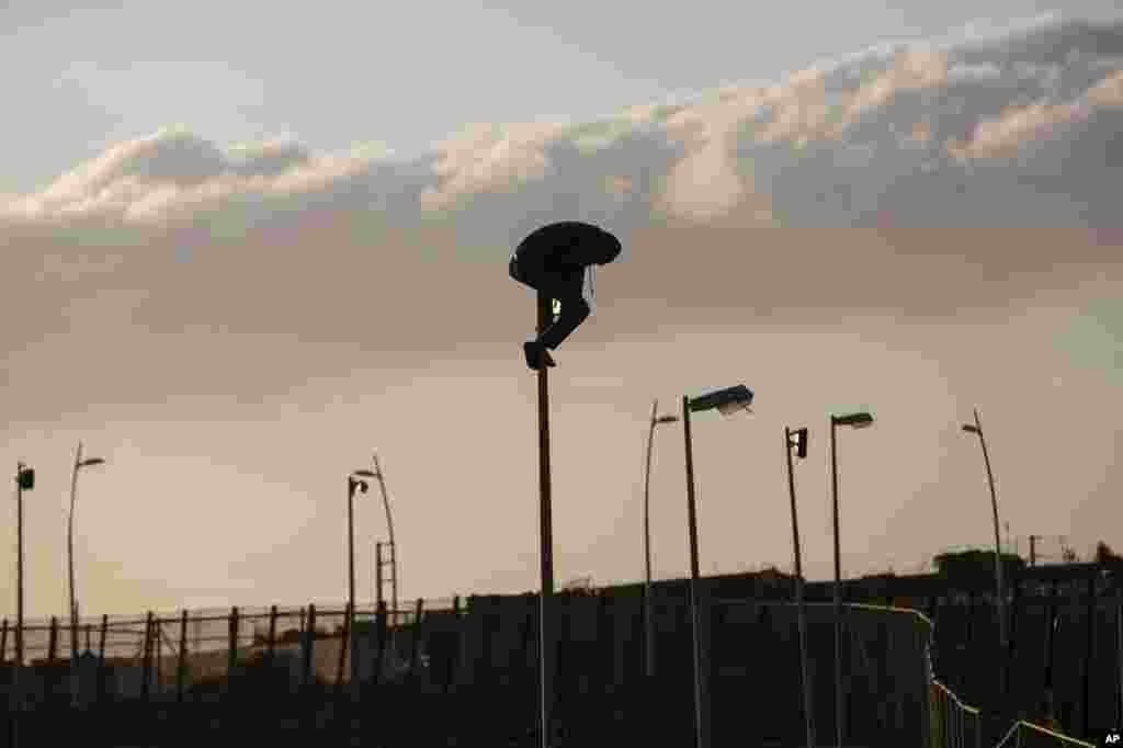 A sub-Saharan migrant sits on top of a pole set in a metallic fence that divides Morocco and the Spanish enclave of Melilla.