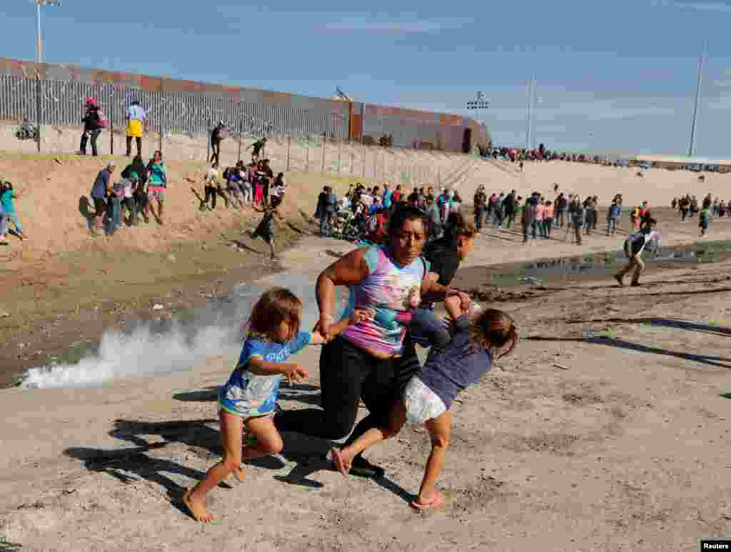 A migrant family, part of a caravan of thousands traveling from Central America en route to the United States, run away from tear gas in front of the border wall between the U.S and Mexico in Tijuana, Mexico, Nov. 25, 2018. U.S. authorities shut the country&#39;s busiest border crossing and fired tear gas into Mexico to repel Central American migrants approaching the border.
