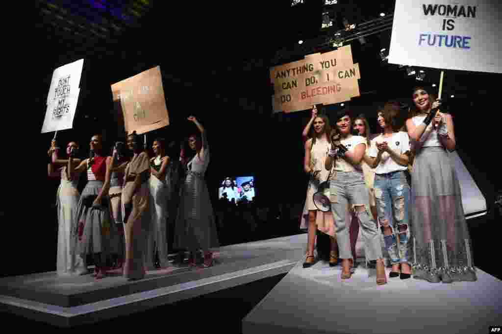 Models carry placards as they present creations by Pakistani designer Hira Ali during the first day of the Pakistan Fashion Design Council Fashion Week in Lahore on March 9, 2018.