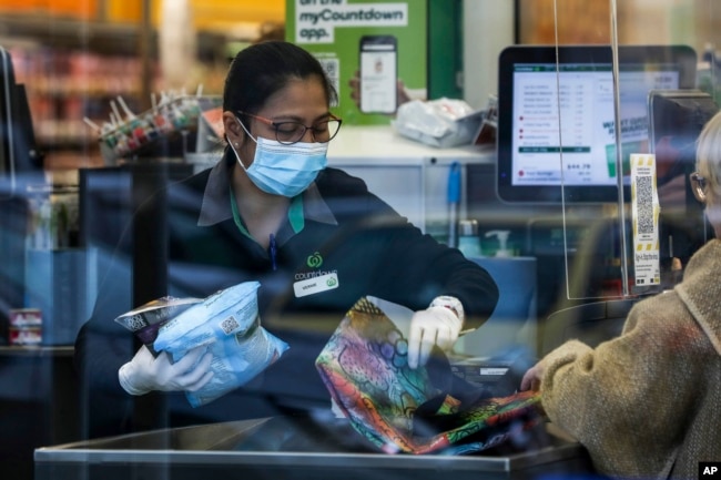 Kasir di sebuah supermarket di Auckland, Selandia Baru, membantu pelanggan memasukkan barang belanjaannya ke dalam tas, Selasa, 17 Agustus 2021. (AP)