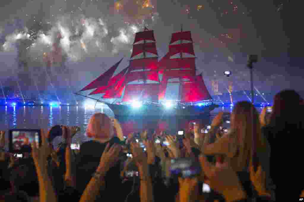 People watch a brig with scarlet sails on the Neva River during the Scarlet Sails festivities marking school graduation in St. Petersburg, Russia.