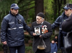Police help Vakhtang Adamashvili, 94, a WWII veteran with a portrait of Soviet dictator Josef Stalin, attend a ceremony in Victory Park marking the 75th anniversary of the Nazi defeat in World War II, in Tbilisi, Georgia, May 9, 2020.