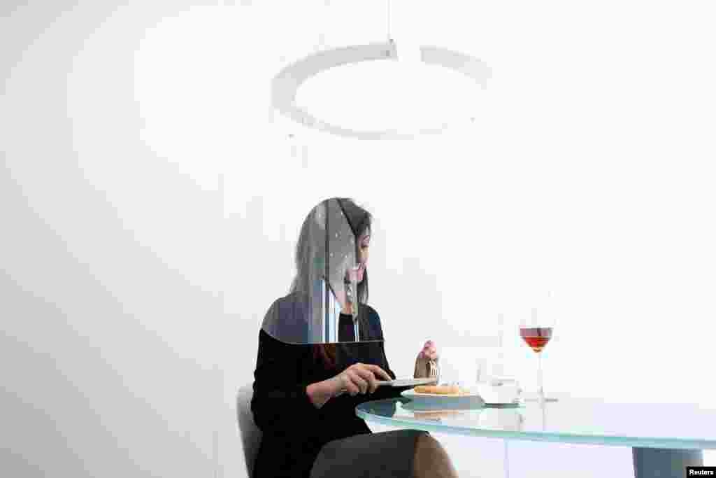 A woman poses under a Plex'Eat prototype plexiglas bubble by designer Christophe Gernigon, which surrounds diners to protect them from the coronavirus, during a presentation in Cormeilles-en-Parisis, near Paris, France.