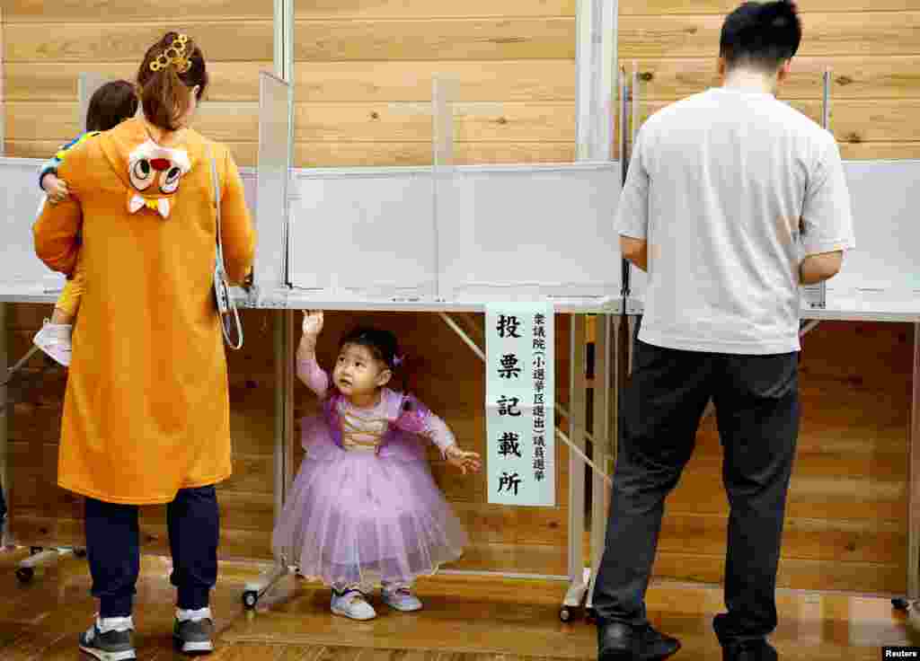 A pistillate   accompanying her children successful  Halloween costume prepares to ballot  during the wide   predetermination  astatine  a polling presumption    successful  Tokyo, Japan.