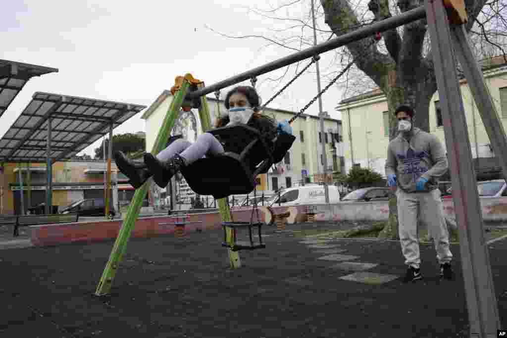Un hombre y su hija, ambos con máscaras faciales, juegan en un columpio en un parque en Roma, Italia.