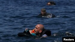 Un refugiado sirio sostiene a su bebé en un salvavidas, mientras nada hacia la costa frente a las isla de Lesbos, en Grecia.