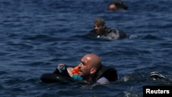 A Syrian refugee holding a baby in a lifetube swims towards the shore after their dinghy deflated some 100m away before reaching the Greek island of Lesbos, Sept. 13, 2015.