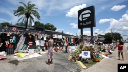This photo taken July 11, 2016, shows visitors taking photos and leaving items at a makeshift memorial outside the Pulse nightclub, the day before the one month anniversary of a mass shooting, in Orlando, Fla. 