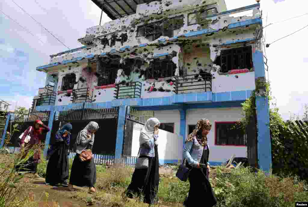 Residents who returned from evacuation centers, walk past a bullet-ridden house believed to have been rented by pro-Islamic State militant group leaders Isnilon Hapilon and Omar Maute before their attack on the region, in Basak, Malutlut district in Marawi, Philippines.