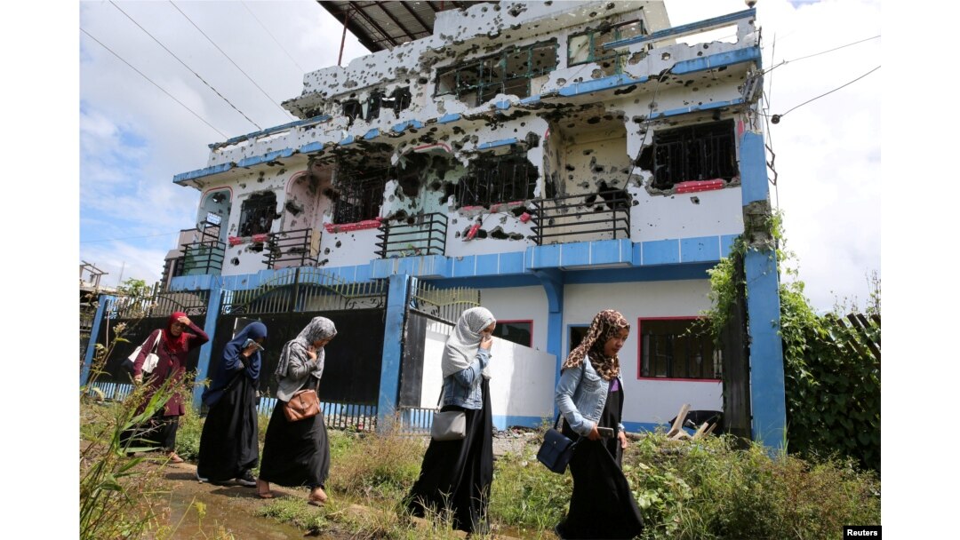 FILE - Residents who returned from evacuation centers walk past a bullet-ridden house believed to have been rented by pro-Islamic State militant group leaders Isnilon Hapilon and Omar Maute before their attack on the region.