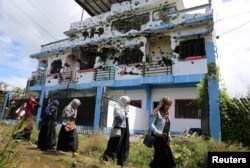 FILE - Residents who returned from evacuation centers walk past a bullet-ridden house believed to have been rented by pro-Islamic State militant group leaders Isnilon Hapilon and Omar Maute before their attack on the region.