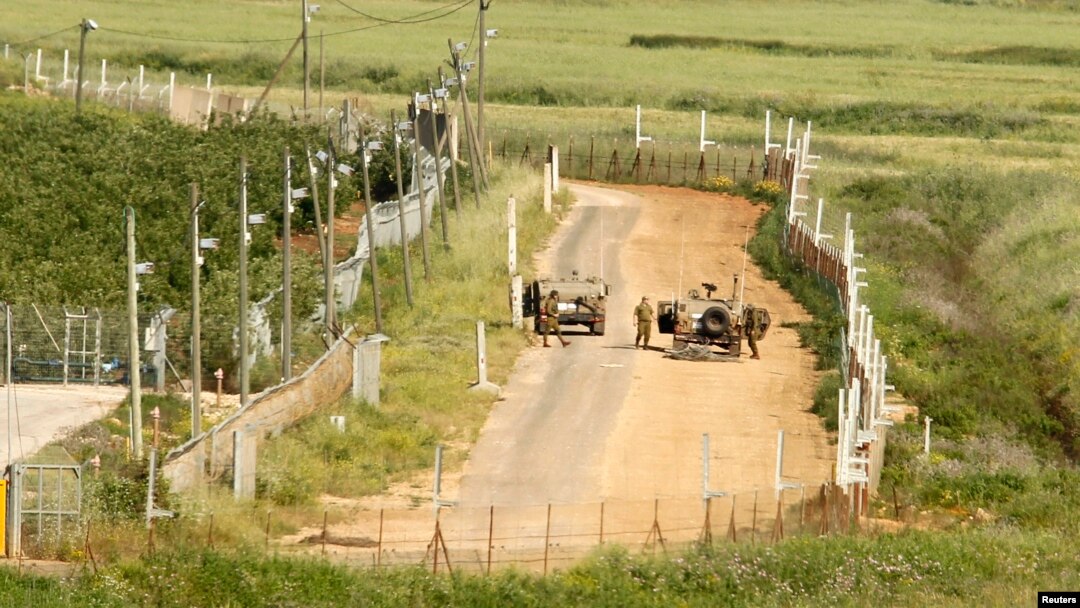 Israeli soldiers stand next to military vehicles along their side of the border with Lebanon, as seen from the southern Lebanese village of Adaisseh, May 4, 2013.