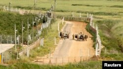 Israeli soldiers stand next to military vehicles along their side of the border with Lebanon, as seen from the southern Lebanese village of Adaisseh, May 4, 2013.