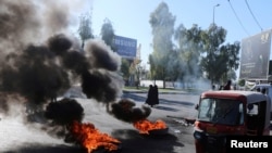 A tuk-tuk drives past burning tires during ongoing anti-government protests in Kerbala, Iraq, Dec. 23, 2019. 