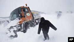 People walk on a snowy road, past stranded intervention vehicles, on the outskirts of Bucharest, Romania, Thursday, Jan. 26, 2012.