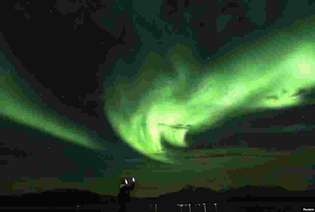 A tourist takes photos of an Aurora Borealis (Northern Lights) over the Bals-Fiord north of the Arctic Circle, near the village of Mestervik, Norway.