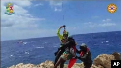 En esta imagen tomada de un video distribuido el domingo 6 de agosto de 2023 por miembros del equipo de Rescate Alpino Italiano, un migrante varado en un arrecife rocoso en la diminuta isla de Lampedusa es ascendido a un helicóptero de rescate. 