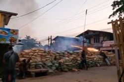 A protester sets off fireworks from behind a barricade while a man, at left, holds a homemade rifle in a clash with security forces in Bago, in this screengrab from Hantarwadi Media video footage taken on April 9, 2021 and provided to AFPTV.