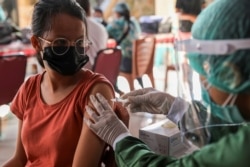 Seorang perempuan disuntik dengan dosis pertama vaksin COVID-19 AstraZeneca, dalam program vaksinasi massal untuk Kawasan Wisata Hijau di Sanur, Bali, 23 Maret 2021. (Foto: REUTERS/Nyimas Laula)