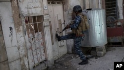 A federal policeman kicks open the door of a house to inspect the interior as fighting against Islamic State militants continues on the western side of Mosul, Iraq, March 29, 2017.