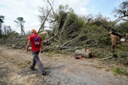 Logan Cunningham of Canary Tree Service of Jacksonville, Fla., walks past tree debris as he waits for more equipment to arrive, in Lake Charles, La., in the aftermath of Hurricane Laura, Aug. 30, 2020.
