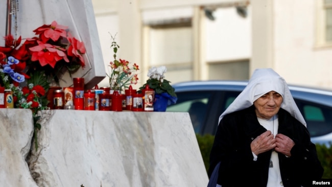 Una monja camina cerca de la estatua del difunto Papa Juan Pablo II afuera del Hospital Gemelli, donde el Papa Francisco está ingresado para continuar el tratamiento de una bronquitis persistente, en Roma, Italia, el 16 de febrero de 2025.