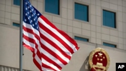 FILE - The American flag flies near the national emblem of China outside of the Bayi Building in Beijing, June 27, 2018. 