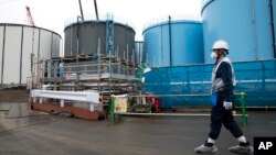 FILE - Employee walks past storage tanks for contaminated water at the tsunami-crippled Fukushima Dai-ichi nuclear power plant of the Tokyo Electric Power Co. in Okuma town, Fukushima prefecture, Japan, Feb. 23, 2017.