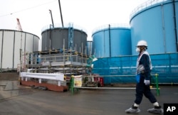 Employee walks past storage tanks for contaminated water at the tsunami-crippled Fukushima Dai-ichi nuclear power plant of the Tokyo Electric Power Co. in Okuma town, Fukushima prefecture, Japan, Feb. 23, 2017.