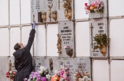 A woman wearing a face mask and gloves touches a niche during the burial of a man who died of the new coronavirus at the South Municipal cemetery in Madrid, on March 23, 2020.