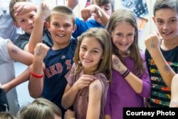 Students and their teacher show temporary tattoos they wear made from the drawing of a letter from Safiyo Noor Hassan, a student in Dadaab Refugee Camp. (Carey Wagner/CARE)